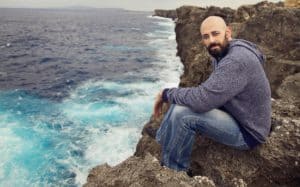 Phil Stacey sitting on the edge of a cliff overlooking a body of water
