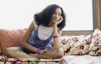 African-American teen girl sitting cross-legged on a couch, staring off into space and daydreaming