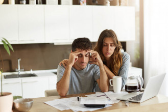 Couple stressed out as they mull over a stack of bills and financial statements on their kitchen table