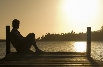 Silhouette of a man sitting on a dock looking out over a lake at sunset