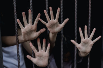 An image of several hands behind bars, so we learn how to stop human trafficking