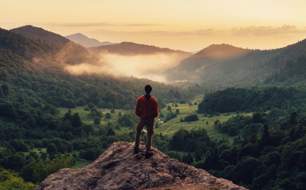 Man standing on top of cliff at sunset