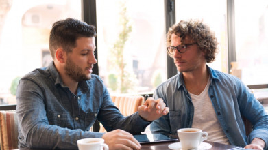 Two young men sitting in a coffee shop having a conversation