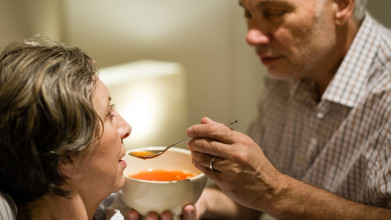 Husband feeding his wife some soup as she lies sick in bed