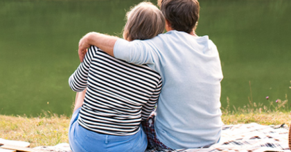 Shown from behind, a couple sitting outside enjoying the view as they have a picnic