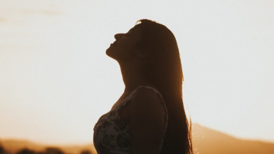 Silhouette of woman standing outside; her head is arched skyward and her eyes are closed like she's enjoying the sunset