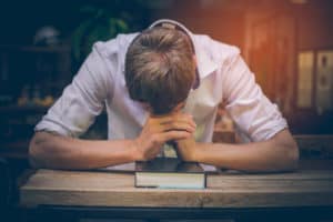 Photo of a pastor, head down, praying over a Bible.