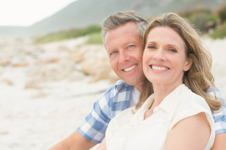 Happy middle-age couple sitting on the beach, smiling for the camera
