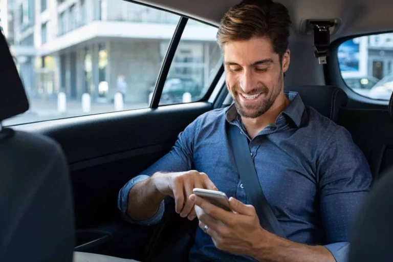 A smiling man in a car types on his phone, sending sweet texts to his spouse to brighten her day.