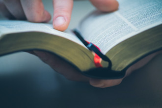 Photo of someone scanning the Bible with their finger.