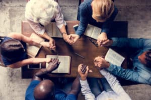 A group of Christian believers gathered around a table, holding hands.