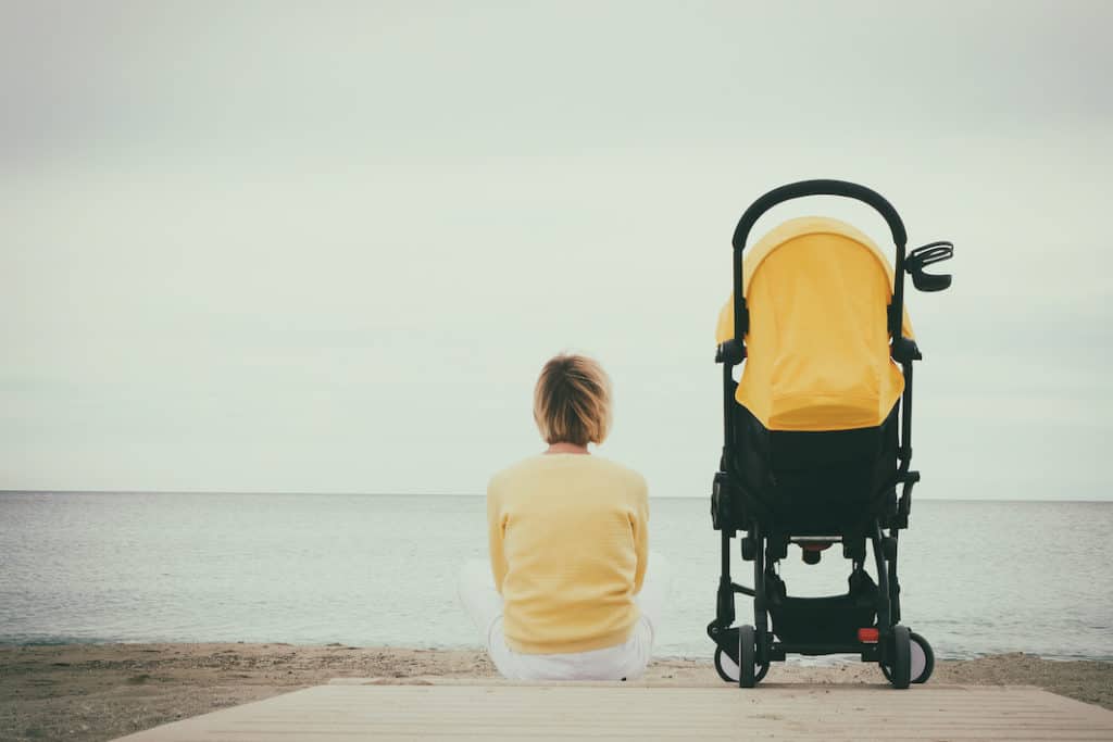 Photo of a woman with a stroller, looking out over the seas.