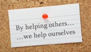 A card with an example of kindness quotes saying, "By helping others... we help ourselves."