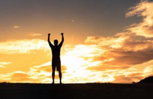 Silhouette of a man with arms raised, backlit by the sunset.