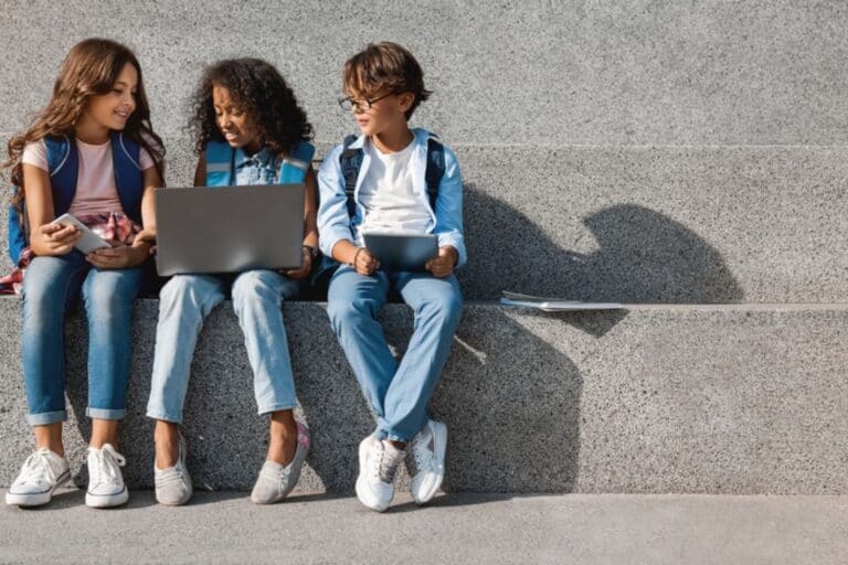 Three teen girls sitting on an outdoor step looking at laptops
