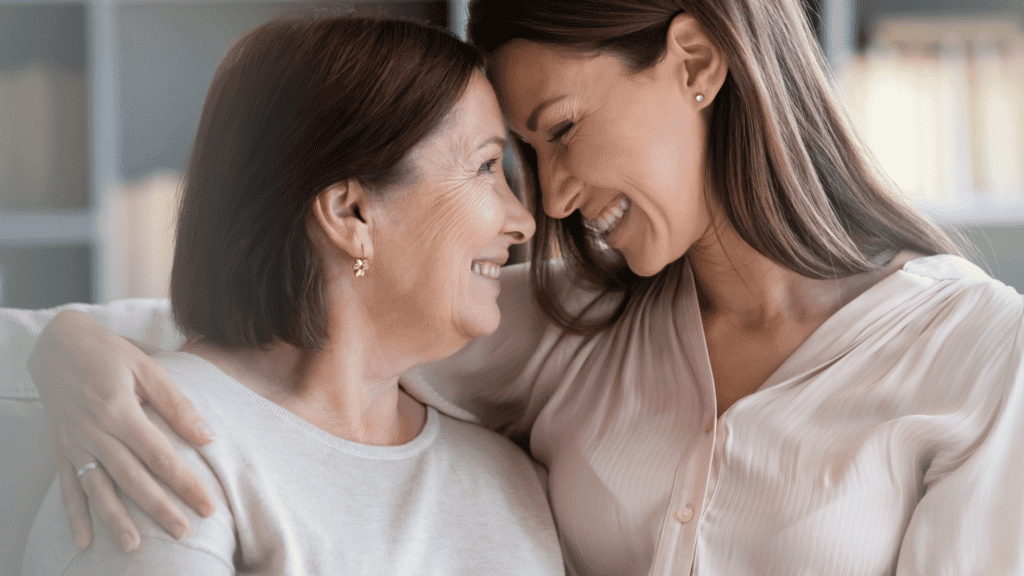 Estrangement, mother and daughter reconciling after two years of family estrangement. Both women sitting on a couch smiling, with the daughter's arm around her mother