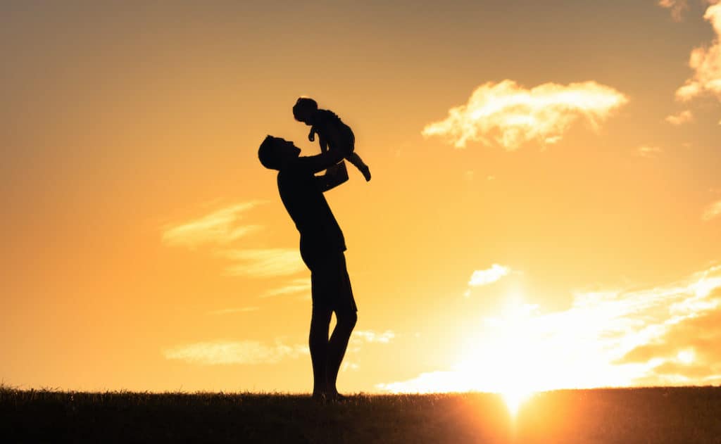 Silhouette of loving father holding up his child at sunset smiling and playing together. This intimacy, love, acceptance and self-giving between the Father and the Son is what Christians understand the “core of the universe” to be.