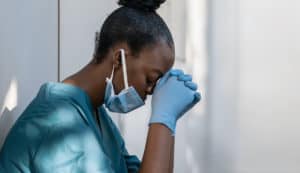 From Planned Parenthood to Pro-Life abortiion worker in blue scrubs kneels and prays.