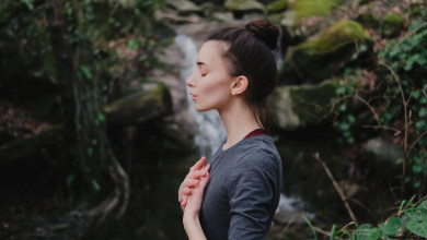 Profile of young woman standing in meditation in front of a waterfall
