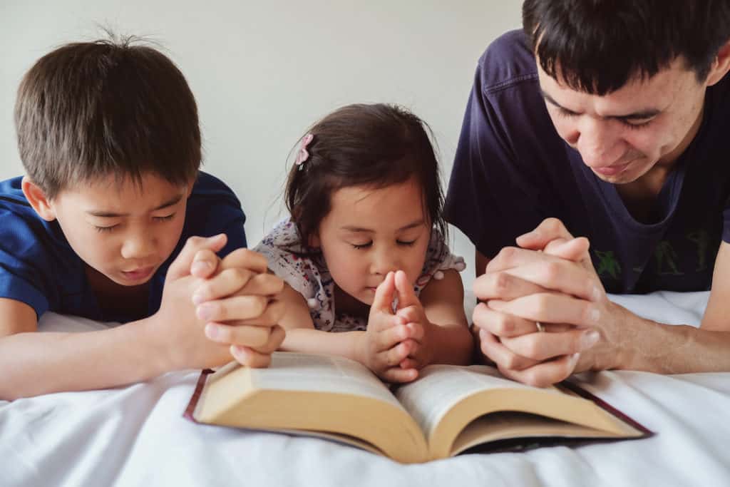 Photo of a man and his children praying over the Bible.