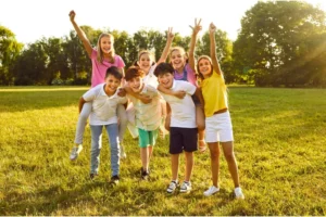 7 school-age children in a group outdoors, smiling with arms raised