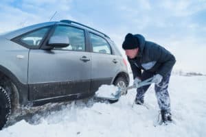 Man shoveling snow to free his stuck car.