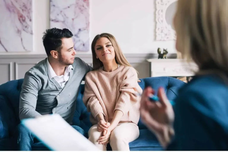 happy couple sits on a couch during a marriage counseling session, demonstrating why marriage counseling can be helpful even if you’re not having issues.