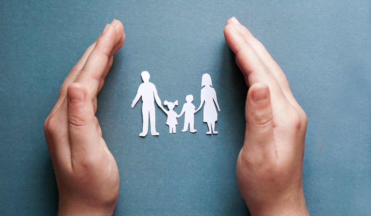 Hands of a boy ground a paper-cut family on blue background for discussing open adoption and family.