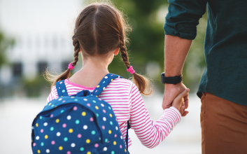 a young girl with a backpack holds the hand of her father