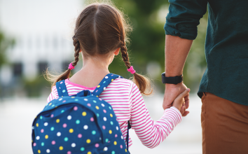 a young girl with a backpack holds the hand of her father
