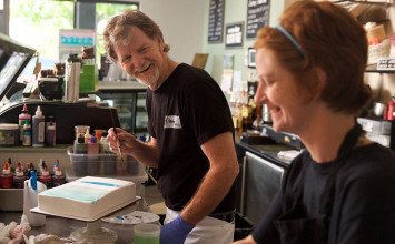 Cake artist Jack Phillips creating a cake in his shop, laughing with a co-worker