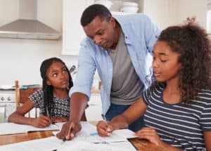 father helping his two daughters do homework.