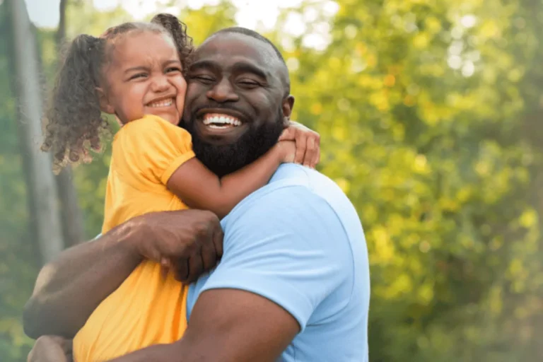 Dad holding and hugging his young daughter, both are smiling
