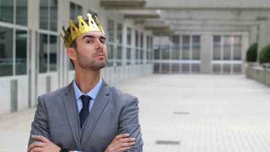 Man in business suit with his arms crossed and wearing a crown, looking haughty