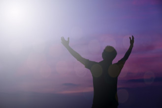 Silhouette of a male raising his arms up toward a purple sky
