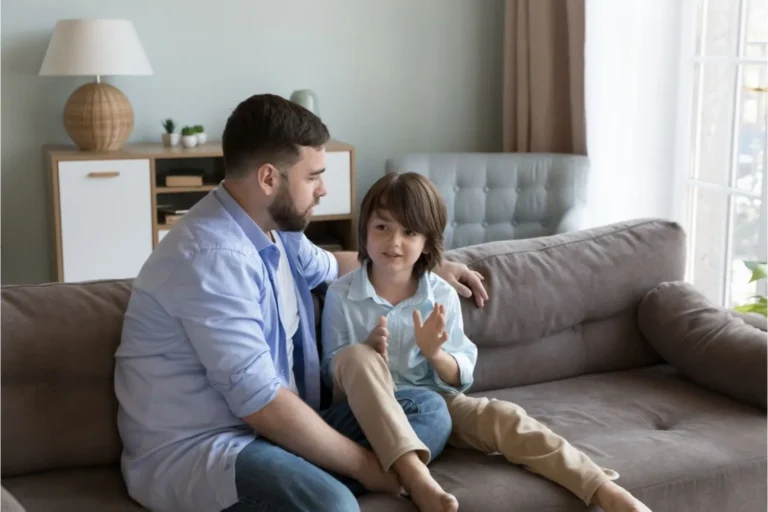 Father and young son sitting together on couch and talking