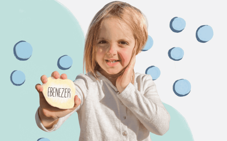 Young girl smiling holding out a rock painted with the word "Ebenezer"