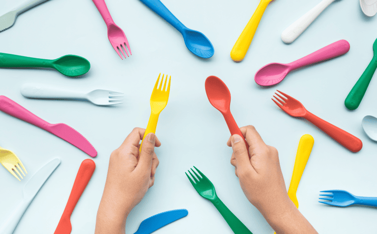 Top view of hand holding colorful spoon and fork with another element on color table