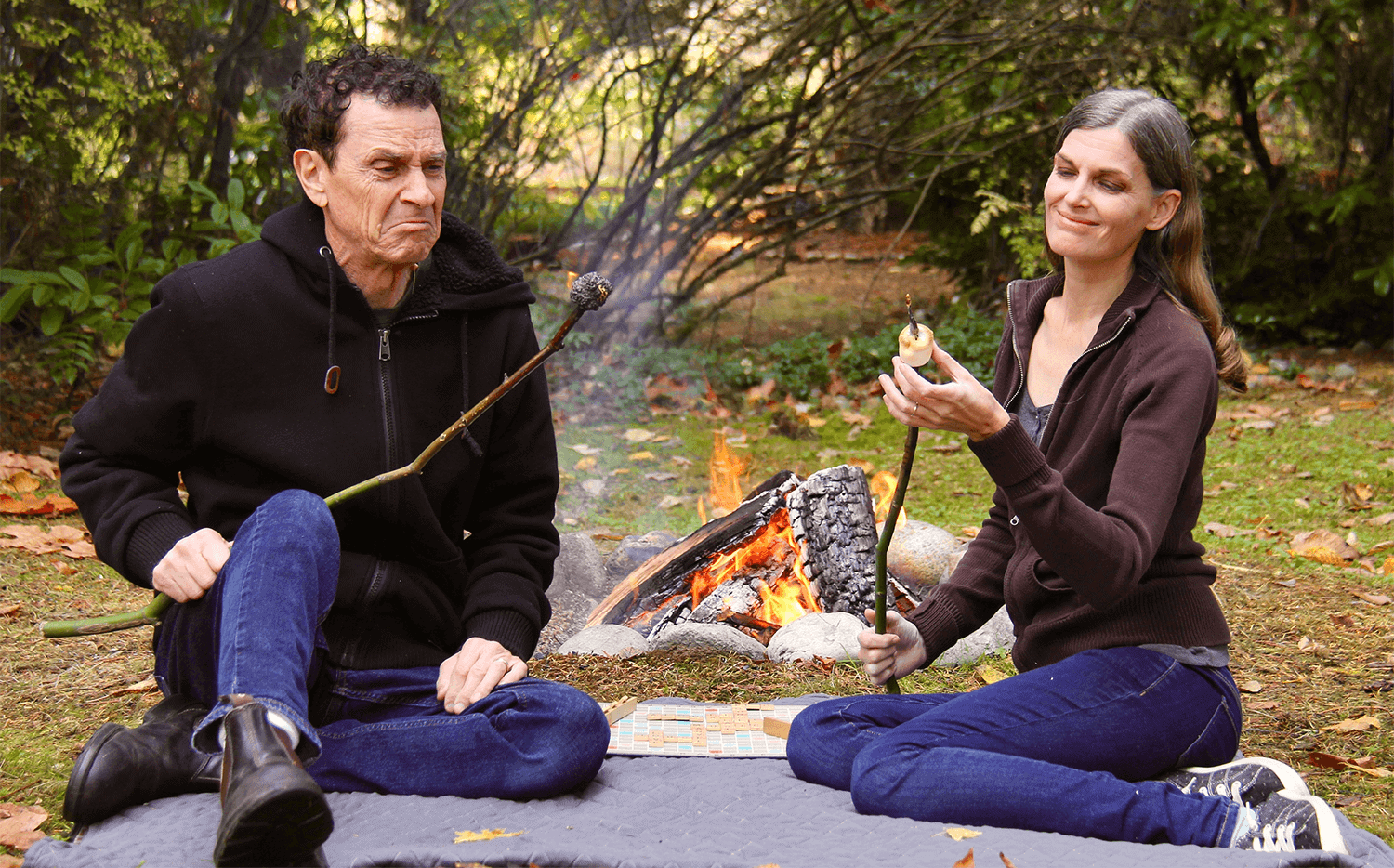 competition in marriage Perry and Julia Springman sitting by a campfire. Perry's marshmallow is burnt and on fire while Julia's marshmallow is perfectly golden.