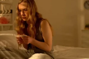 Teen girl sitting in her bedroom, looking at a positive pregnancy test
