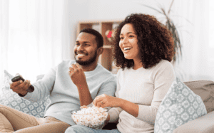 people and leisure concept - african american couple with popcorn watching tv at home