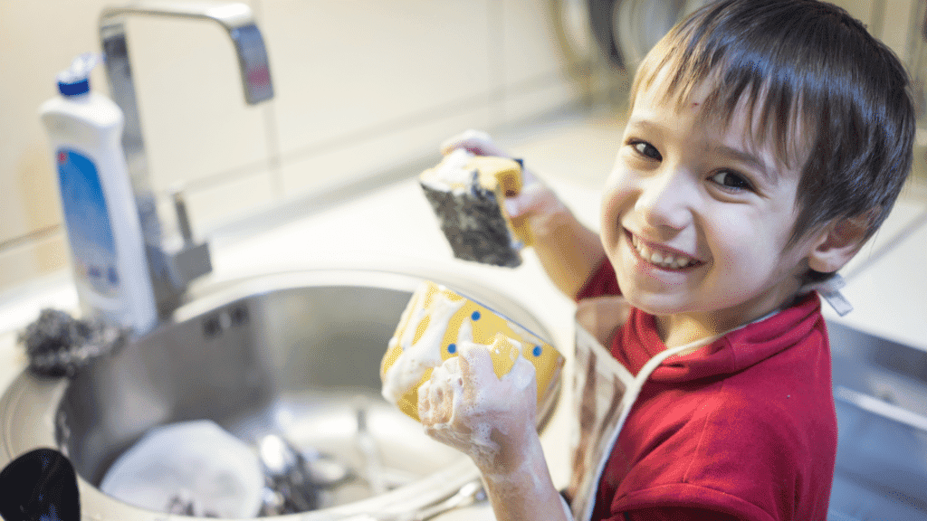 kids doing chores. Little boy with a big smile, in a red shirt, doing the dishes as his daily chore