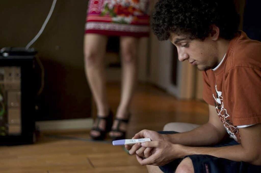 Teen boy holding a pregnancy test and looking uncertain.