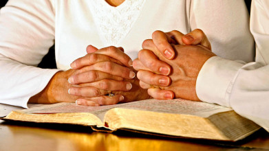 Praying hands of married couple on Bible