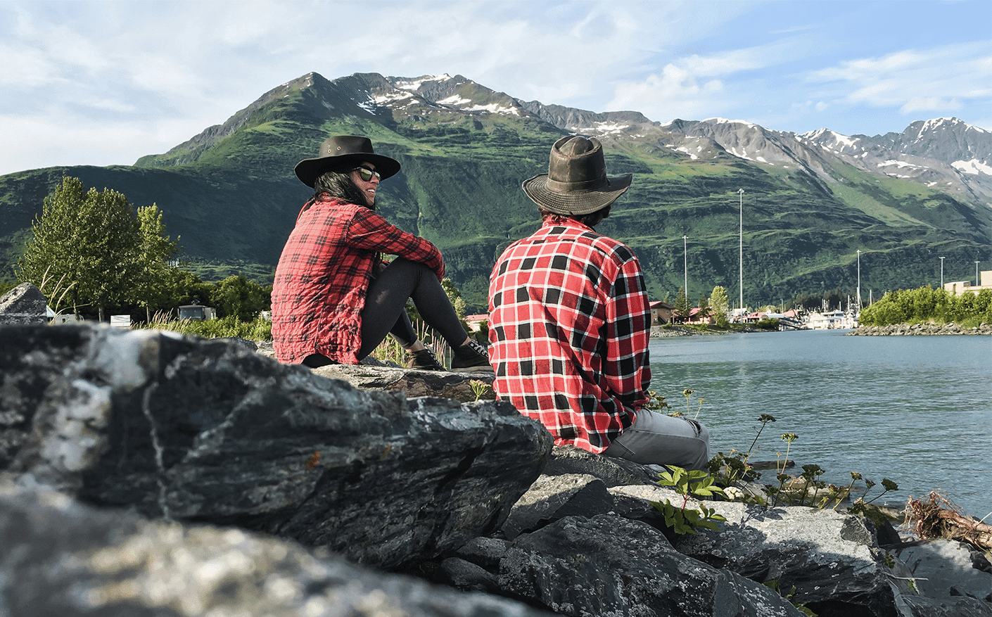 fishing for connection - Couple in flannel sitting on rocks near water in Alaska