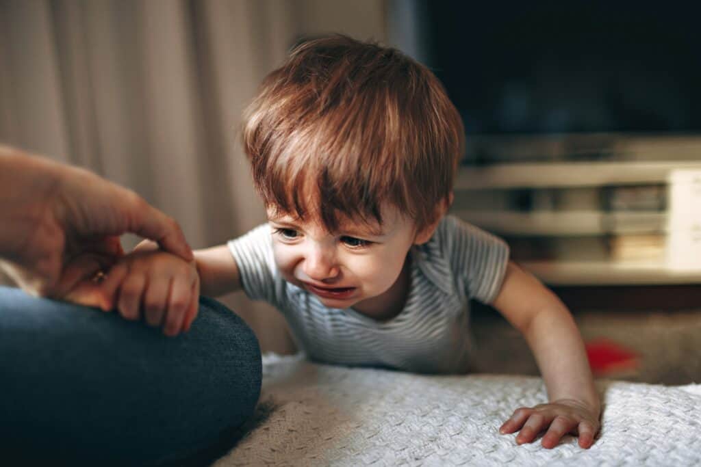 Toddler crying on bed near parent's hand