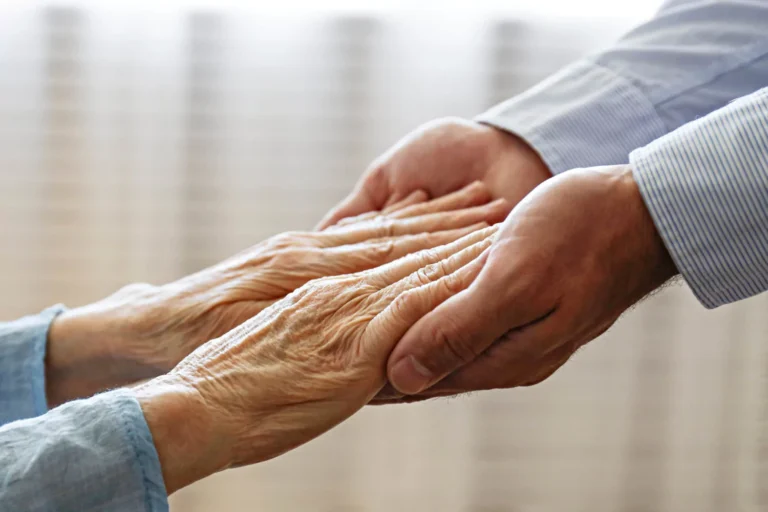 Close-up of a younger person gently holding the hands of an elderly person.
