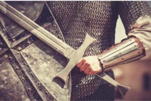 A mighty warrior gripping a medieval sword, clad in chainmail armor and a sturdy bracer, with a weathered shield in the foreground. The image conveys strength, courage, and readiness for battle