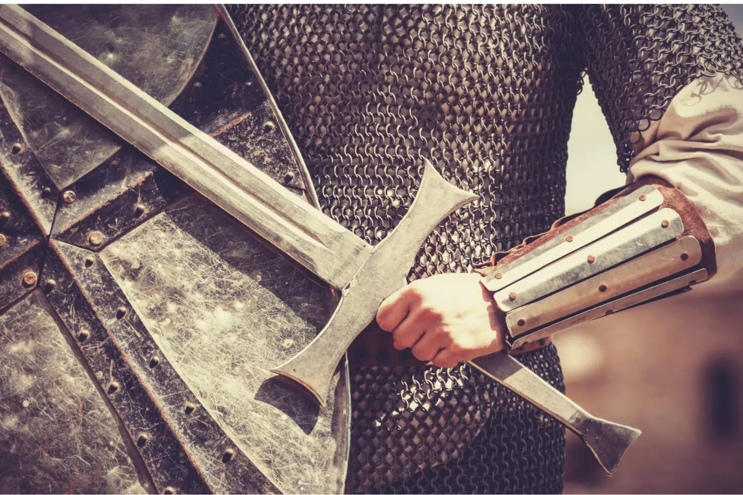 A mighty warrior gripping a medieval sword, clad in chainmail armor and a sturdy bracer, with a weathered shield in the foreground. The image conveys strength, courage, and readiness for battle