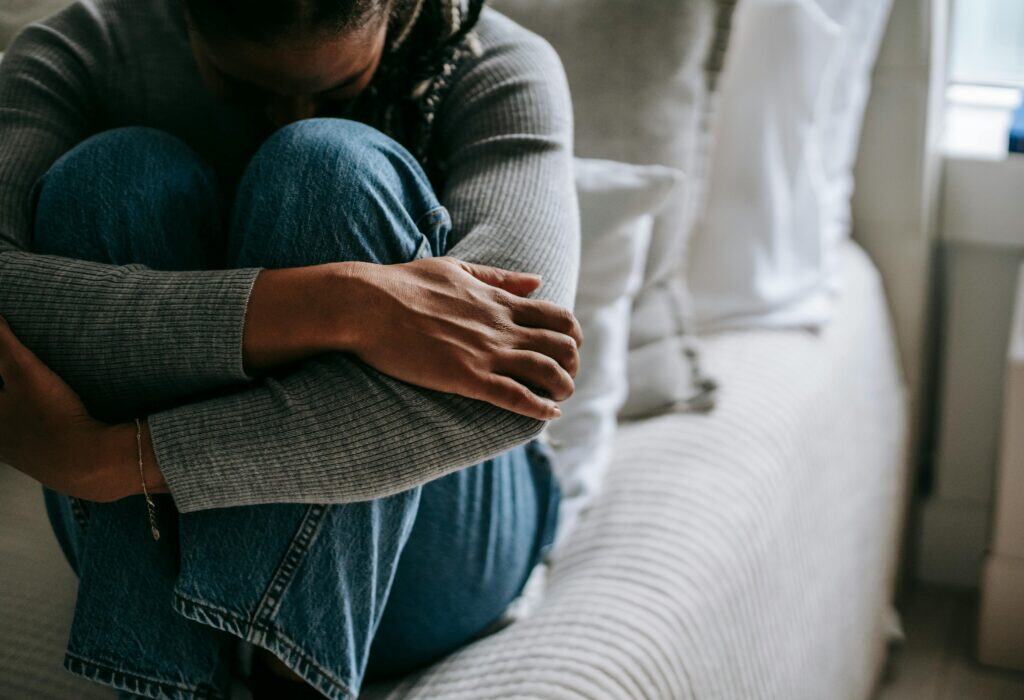 woman sitting on bed arms wrapped around knees upset sad